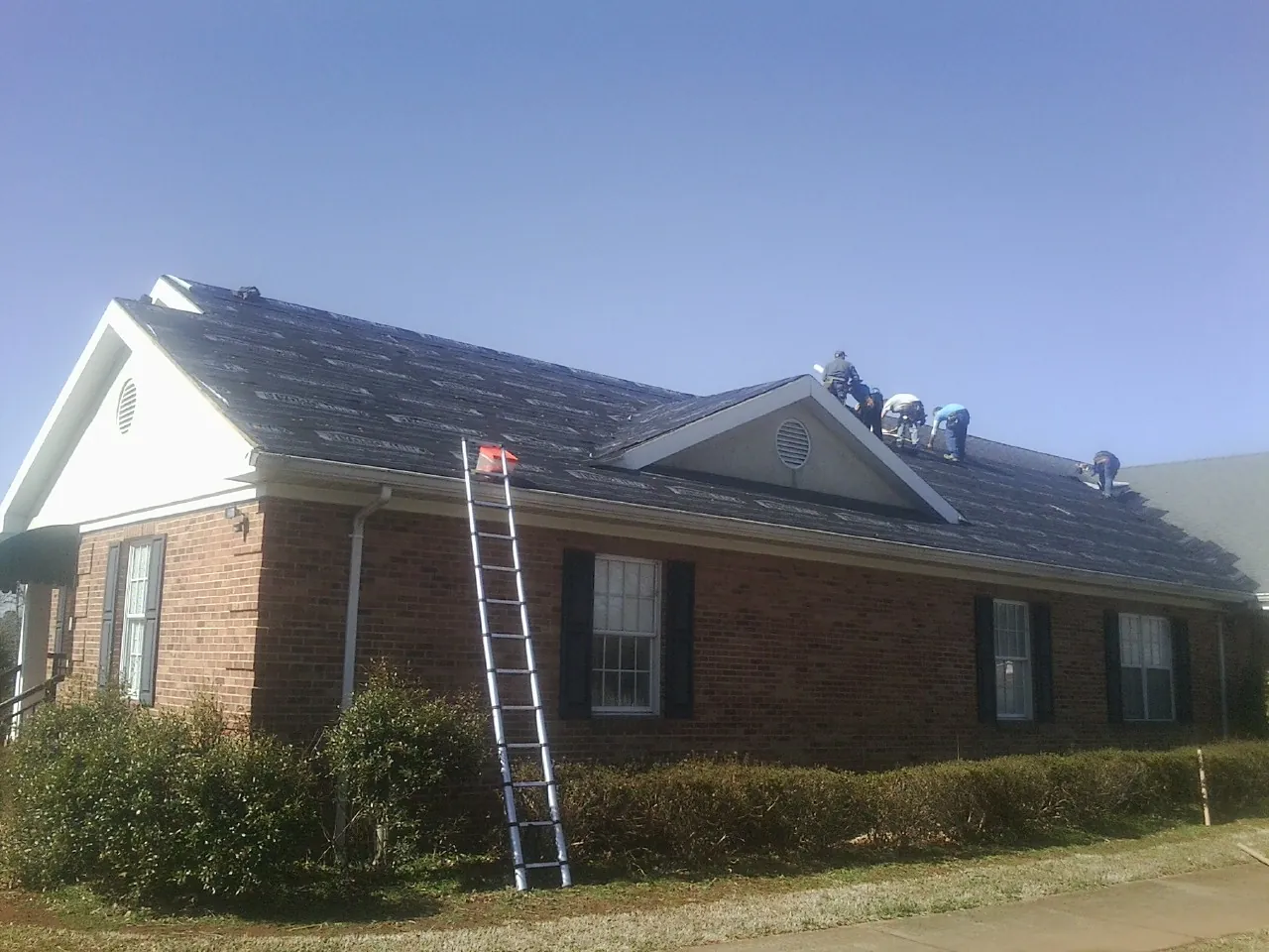 Crew tearing shingles off a brick ranch roof with a ladder set — Emergency Roof Repair work by our crew in Park