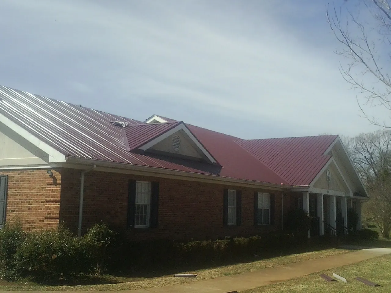 Red metal roof with gabled entries on a long brick building, from a Hail Damage Roof Repair job in Park