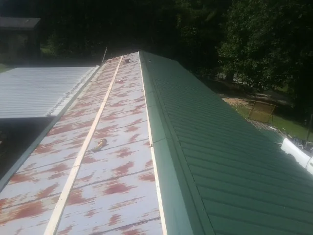 Old rusted panels beside newly installed green metal roofing — Wind Damage Roof Repair by Roofing Brothers in Park