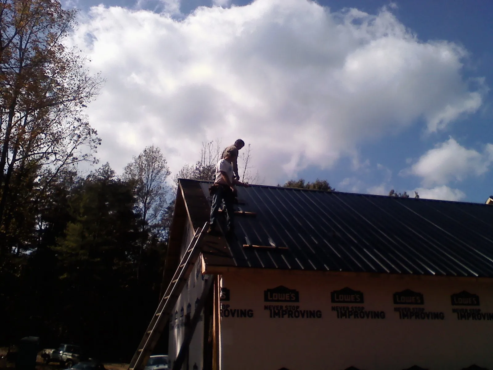 Roofer fastening dark metal panels high against a cloudy sky, from a Roof Inspection job in Park
