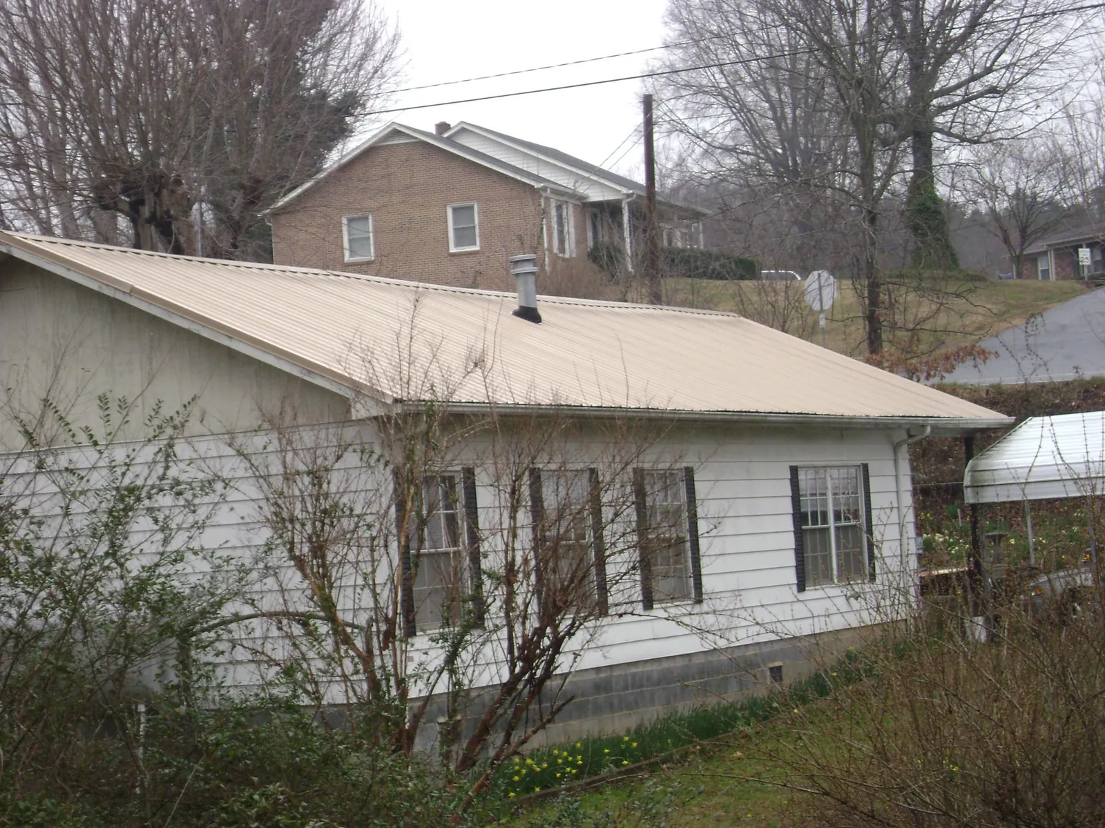 Tan metal roof on a white sided house set into a hillside — Commercial Roofing by Roofing Brothers in Park